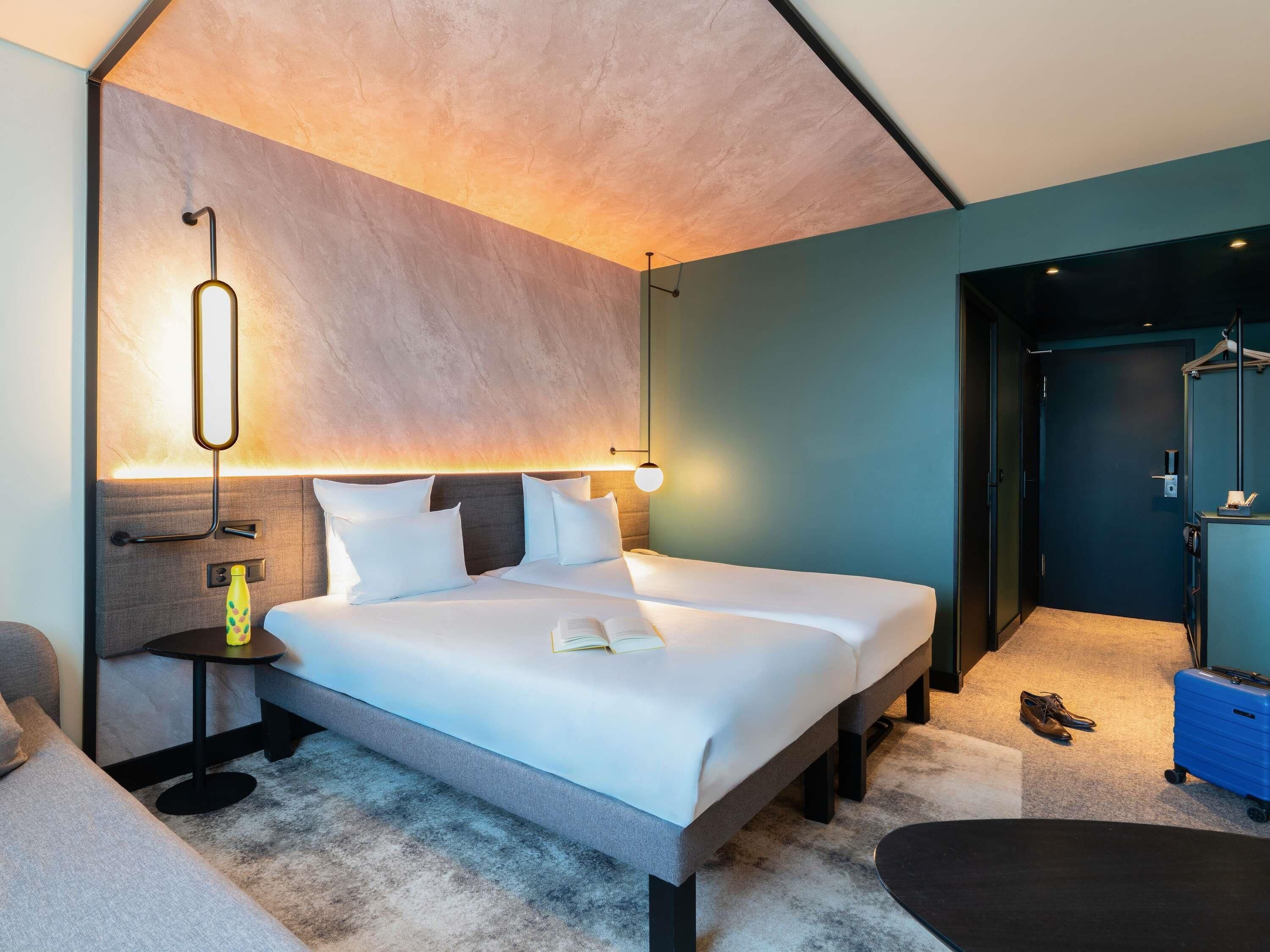 A modern hotel room with a large bed, bedside tables, a reading lamp, and a view of the hallway.