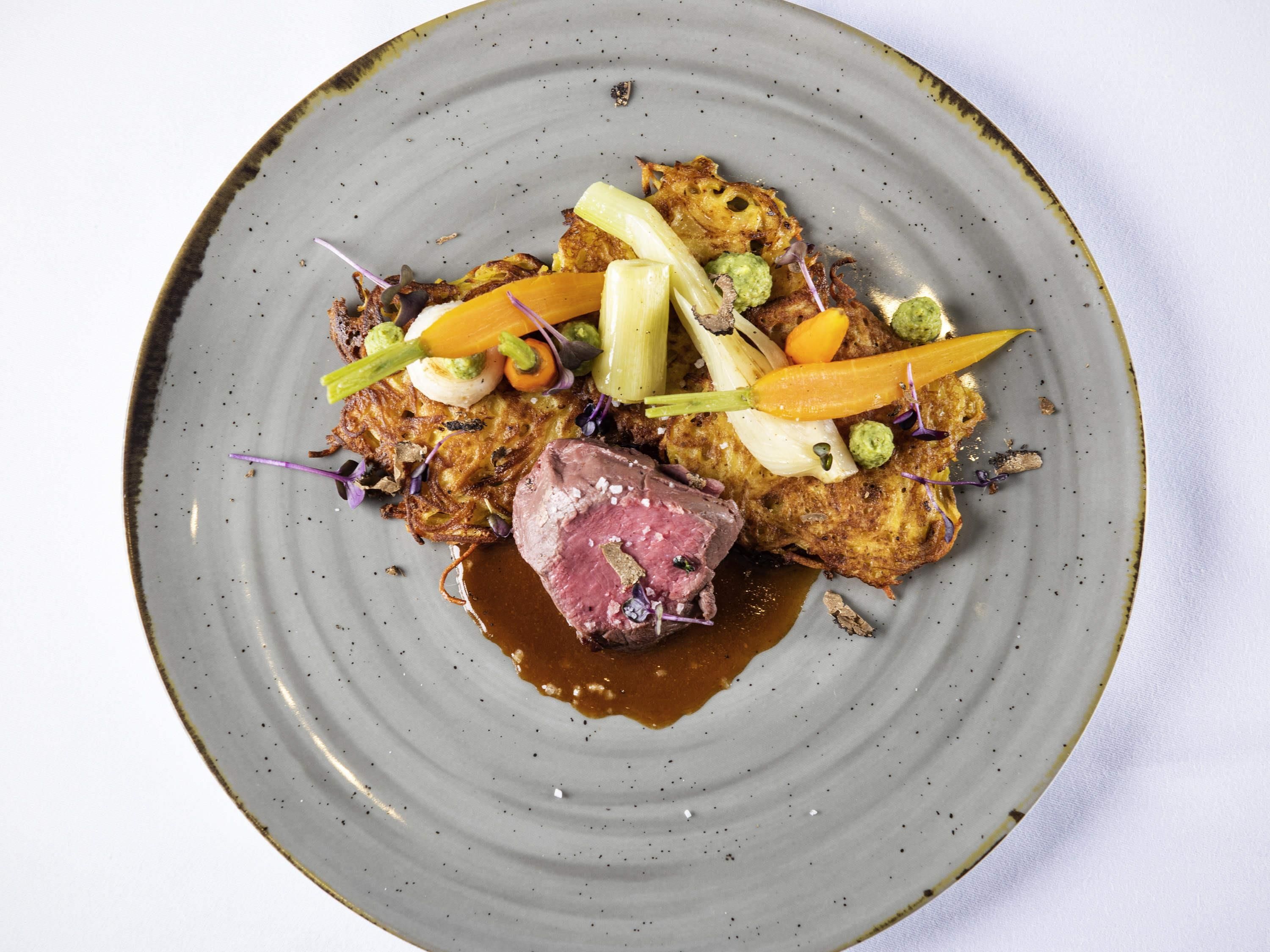 Un plato de comida con un bistec, verduras y salsa.