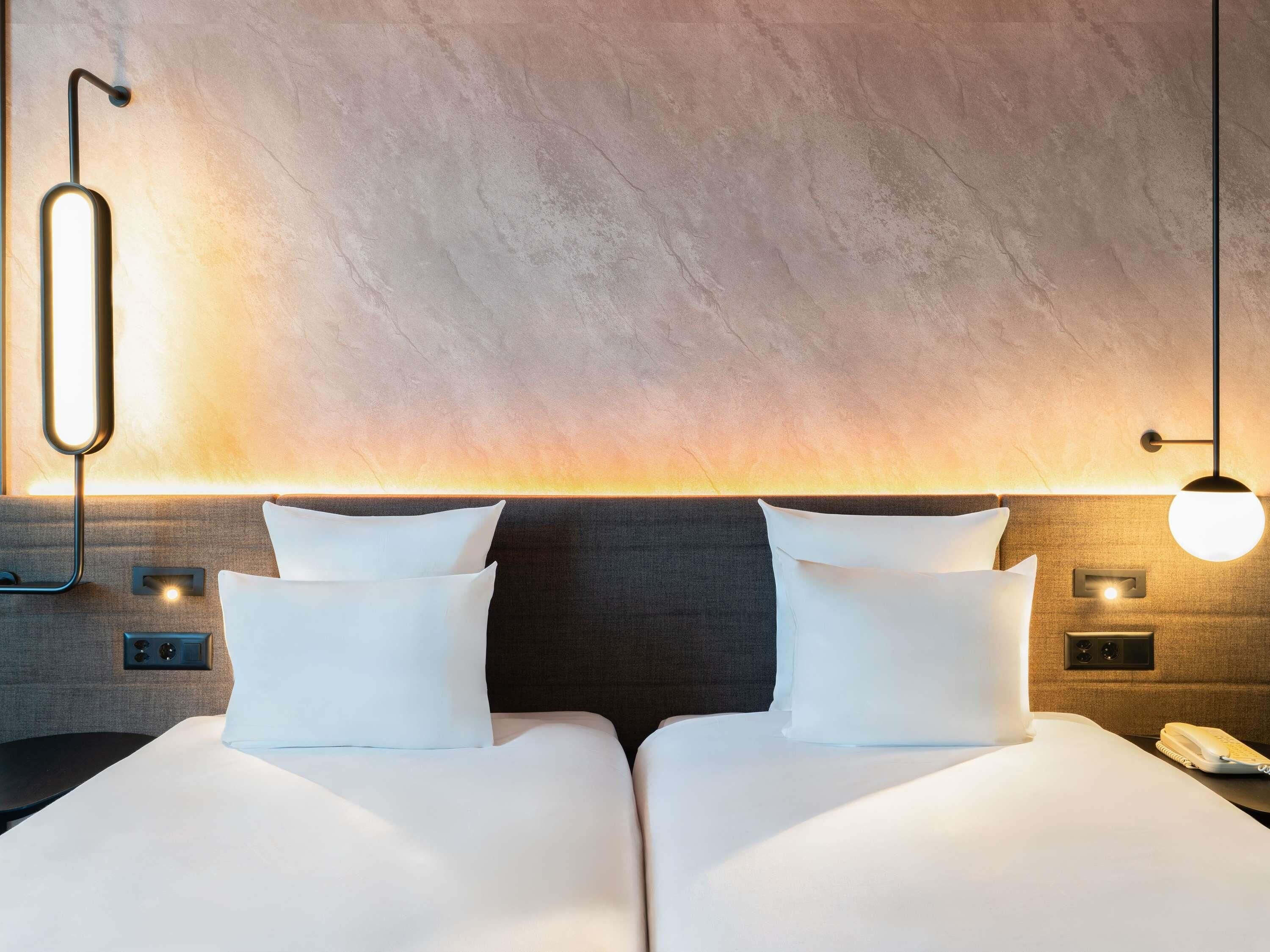 A hotel room with a double bed, a nightstand, a phone, and a wall-mounted light fixture.