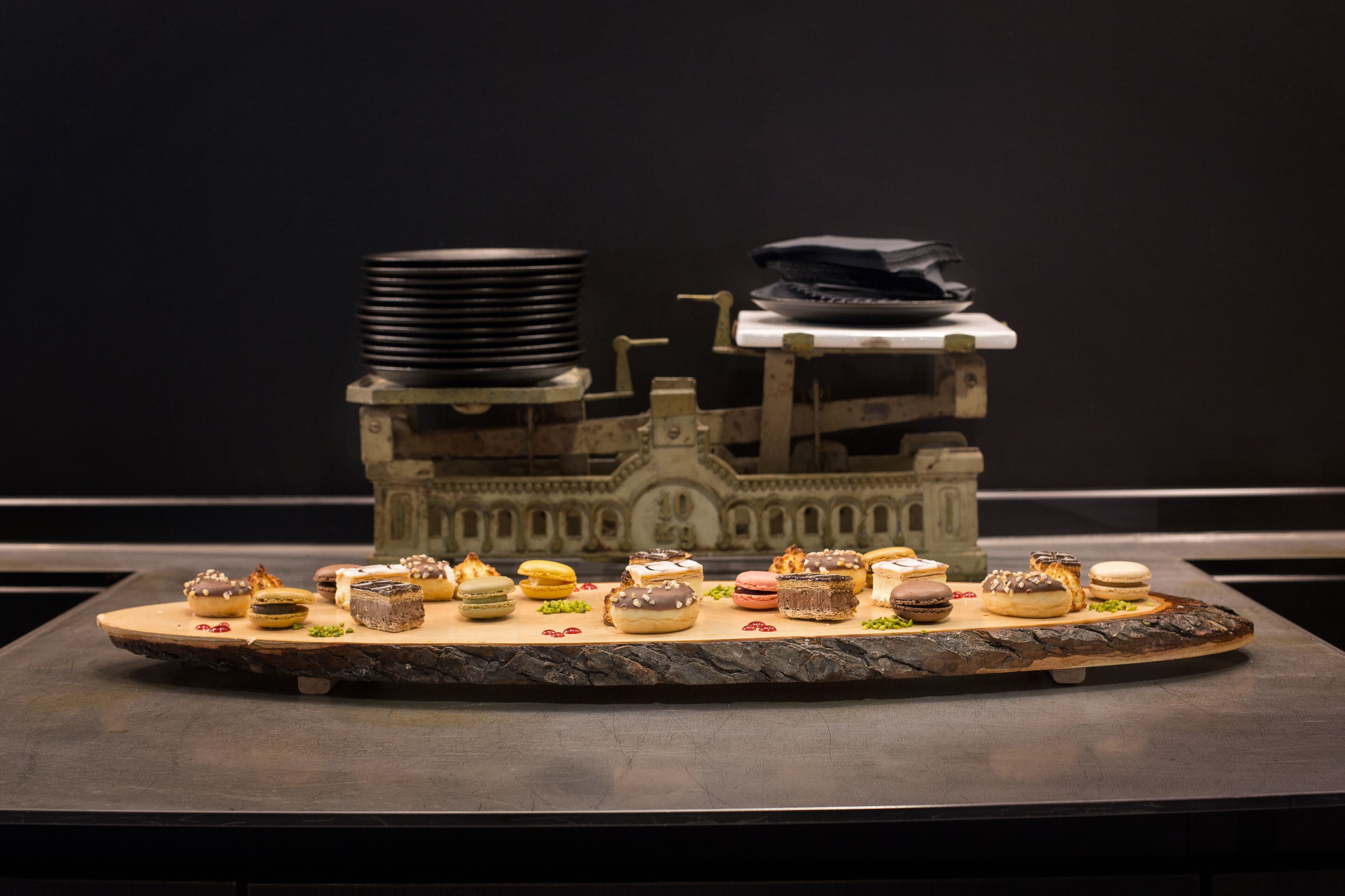 A dessert display on a wooden board with various pastries and a model building in the background.
