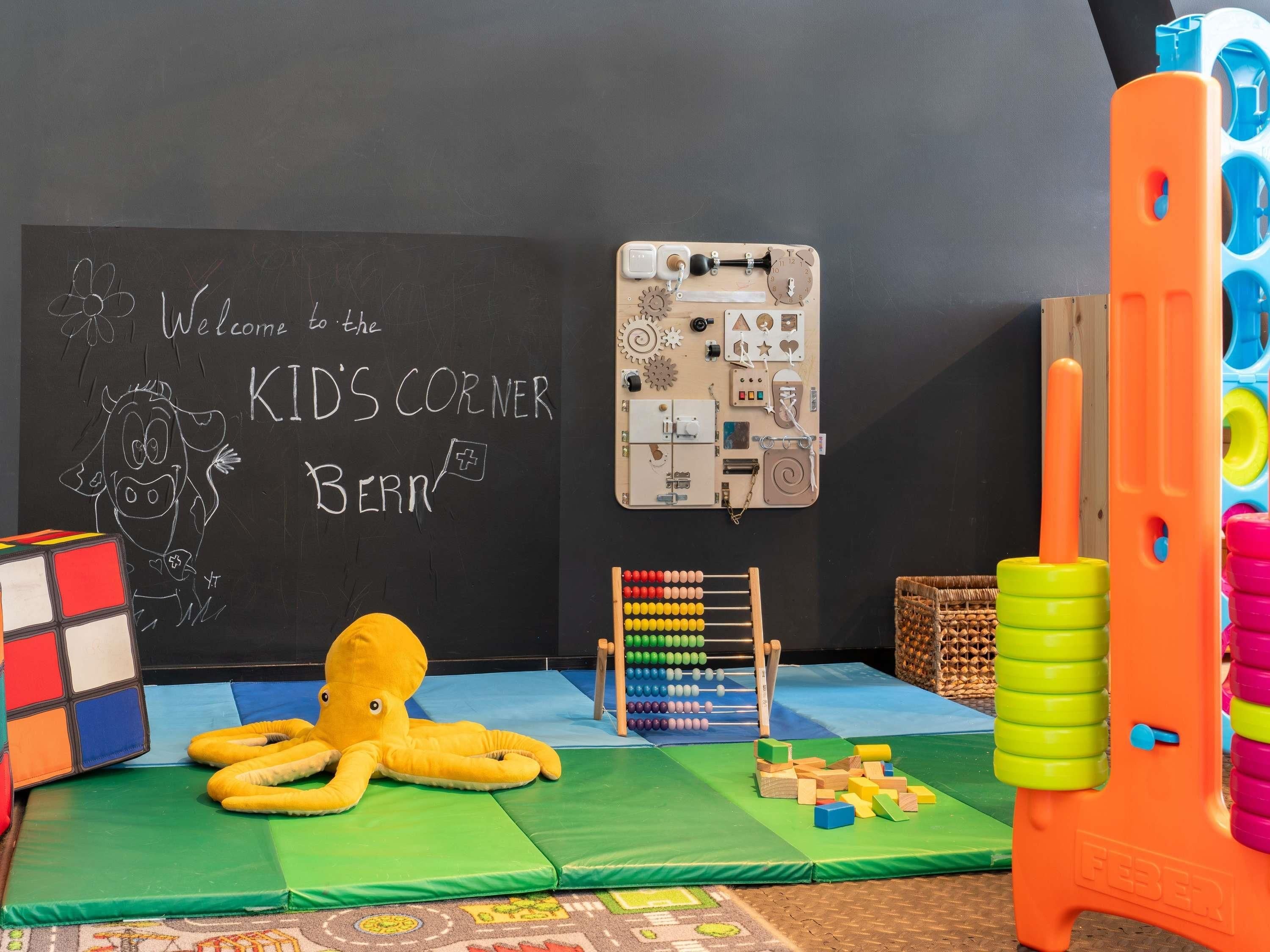 Ein Kinderspielbereich mit einer Schiefertafel, einem Oktopus-Spielzeug, Bauklötzen und einer hölzernen Spielanlage.