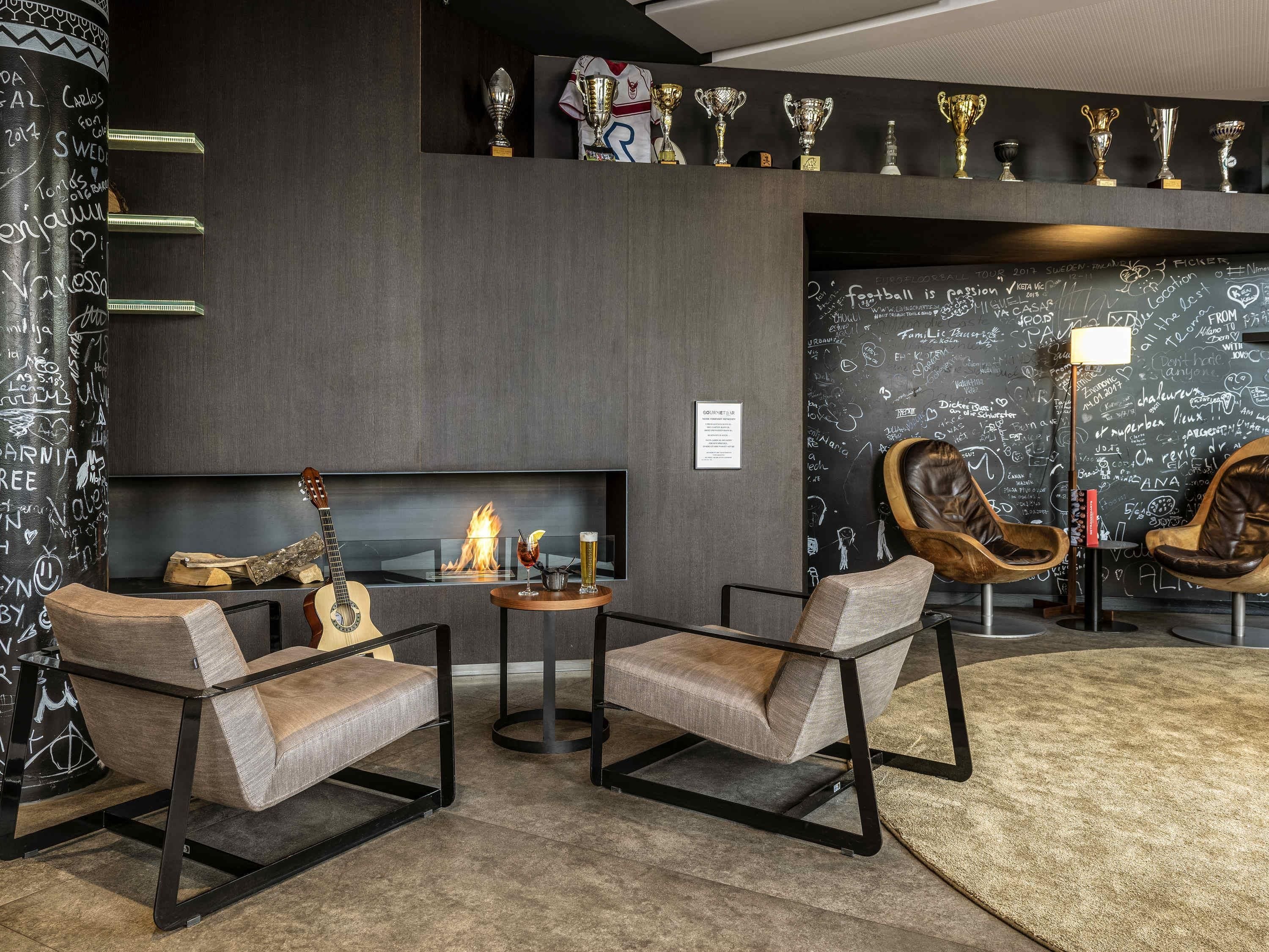Un salon moderne doté d’une cheminée, de fauteuils en cuir, d’une guitare et d’un mur orné de trophées et de notes manuscrites.