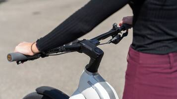 Gros plan sur le guidon d’un vélo et sur une personne portant un haut noir et un pantalon bordeaux.