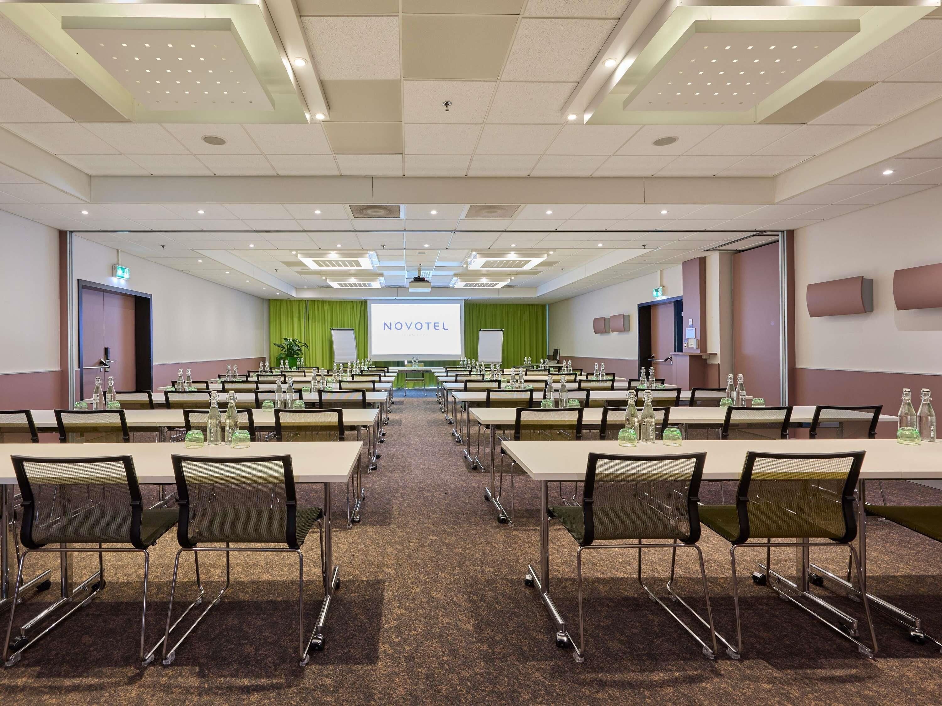A conference room with tables, chairs, a projection screen, and a stage.