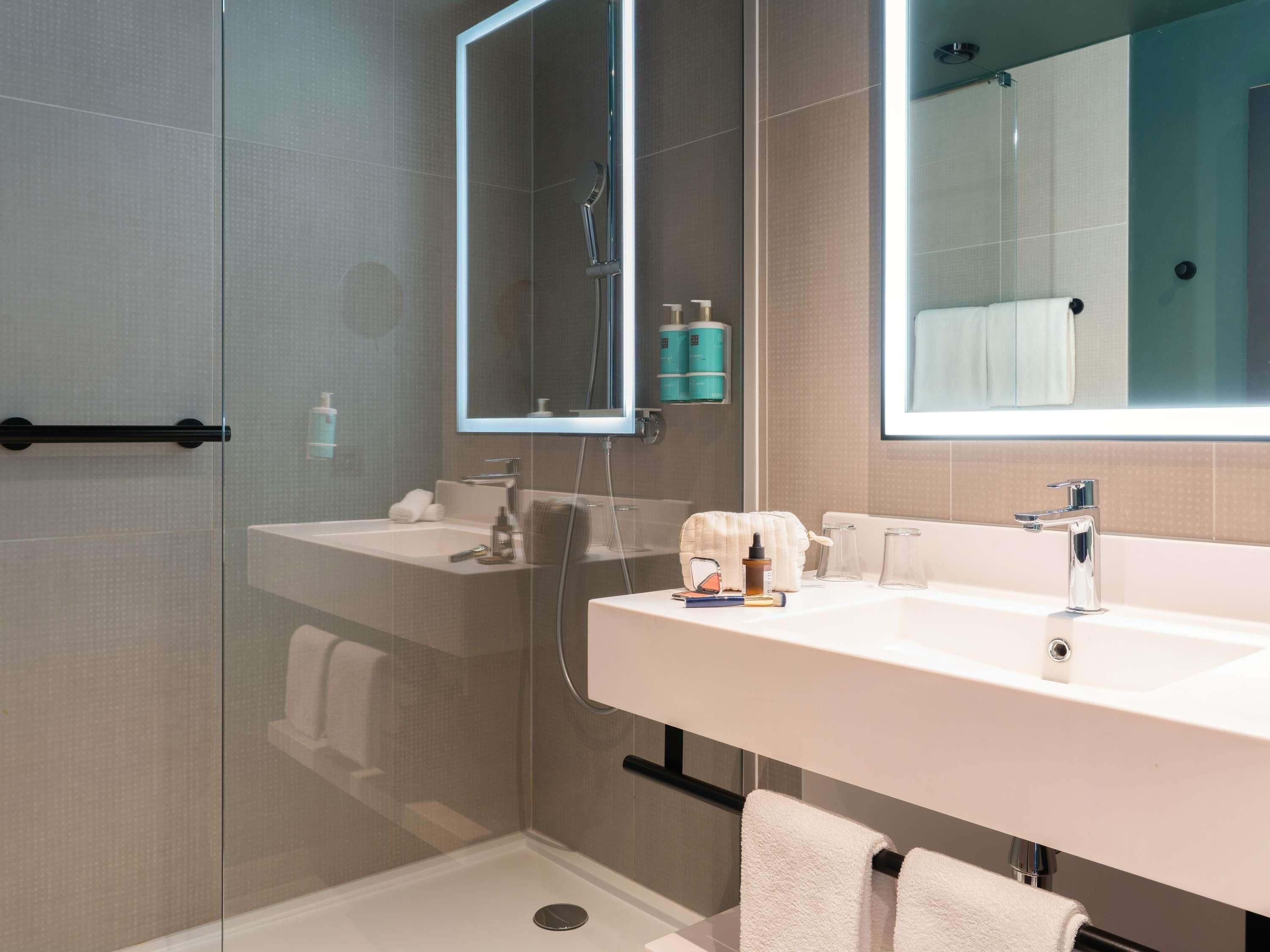 Un baño moderno con cabina de ducha de vidrio, dos lavamanos y un espejo grande.