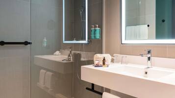 Un baño moderno con cabina de ducha de vidrio, dos lavamanos y un espejo grande.
