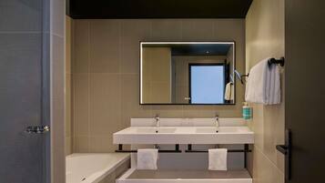 A modern bathroom with a large mirror, two sinks, a bathtub, and a towel rack.