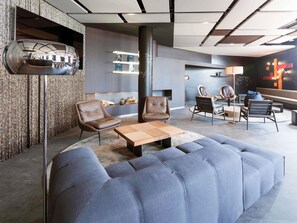 A modern lounge area with leather chairs, a wooden coffee table, and a large blue sofa. - Novotel Bern Expo (Bern)