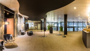 Un moderno hall de hotel con techo curvo, un mostrador de recepción, un área de descanso con sillones y un ventanal con vistas a la ciudad.