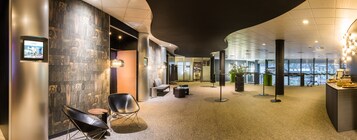 A modern hotel lobby with a curved ceiling, a reception desk, a seating area with chairs, and a large window offering a city view.