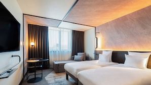 Habitación de hotel con una cama grande, un escritorio, una silla, un televisor y una ventana con cortinas.