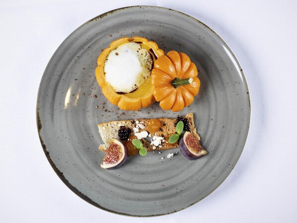 A plate with a stuffed pumpkin, a slice of bread with figs and blackberries, and a small dollop of cream.
