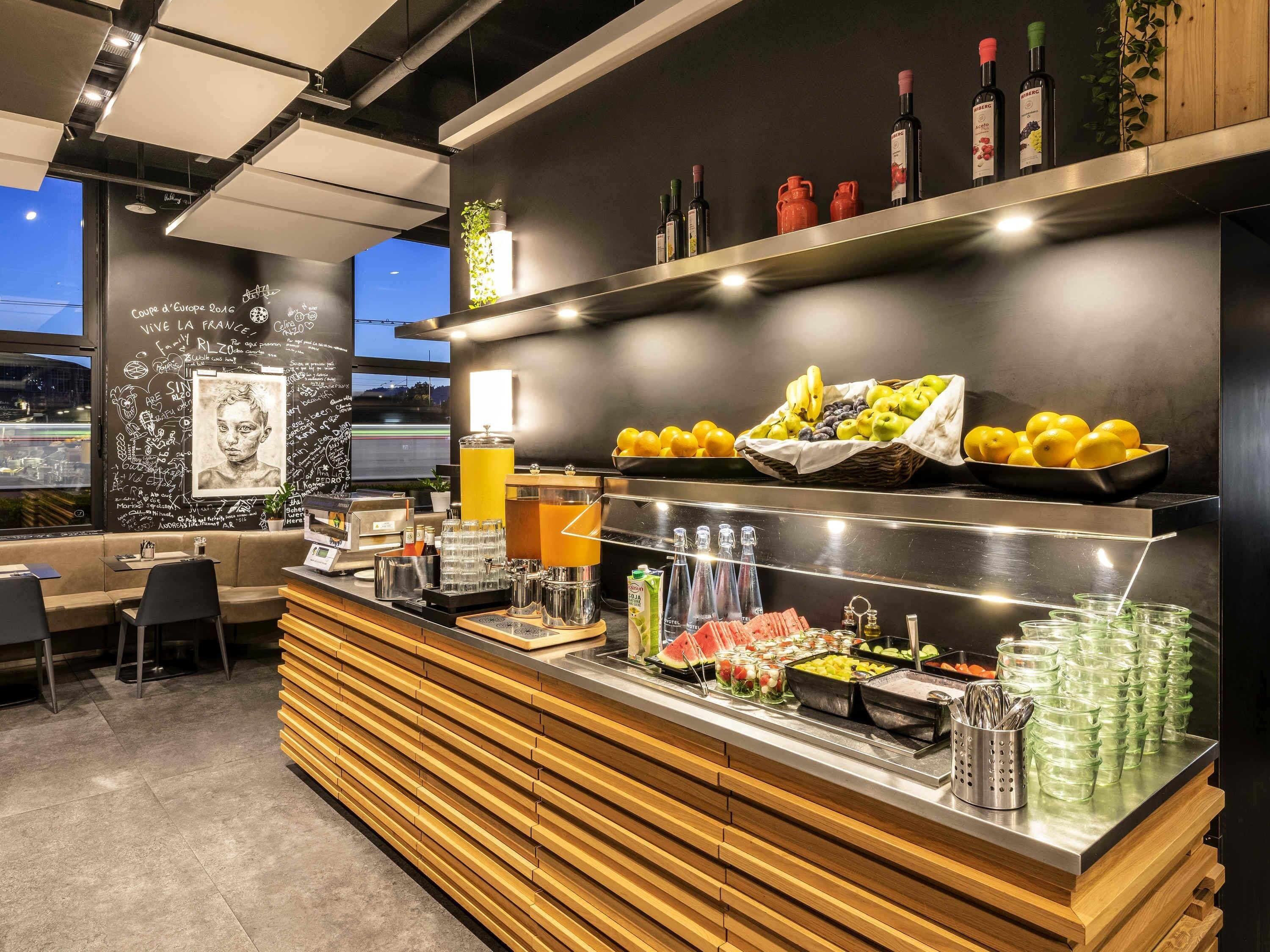 Zona de bar con diversas bebidas, frutas y una pizarra con textos escritos.