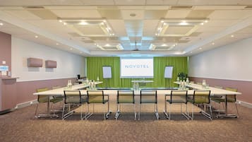 Une salle de conférence avec une longue table, des chaises, un écran de projection et un fond vert en guise de décor.