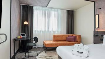 Une chambre d’hôtel moderne équipée d’un lit, d’un bureau avec un ordinateur portable, d’un canapé et d’une grande fenêtre avec des rideaux.