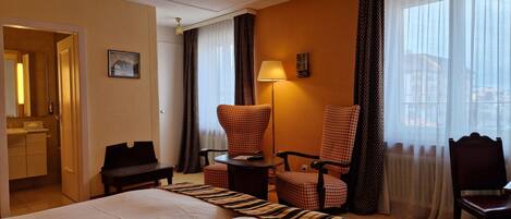 A hotel room with a large bed, two armchairs, a small table, and a lamp.