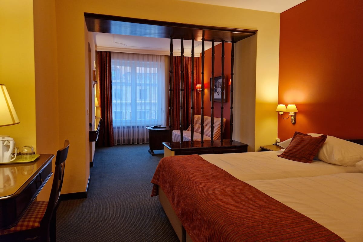 Habitación de hotel con cama, escritorio, silla, mesita de noche y ventana con cortinas.
