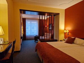 A hotel room with a bed, a desk, a chair, a nightstand, and a window with curtains.