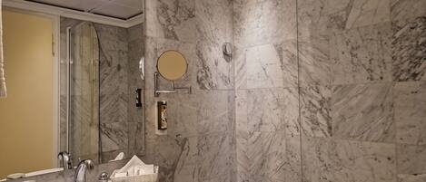 Un baño con pared de mármol, lavamanos, espejo y bañera.
