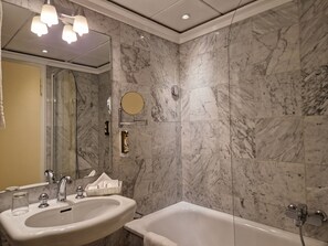 A bathroom with a marble wall, a sink, a mirror, and a bathtub.