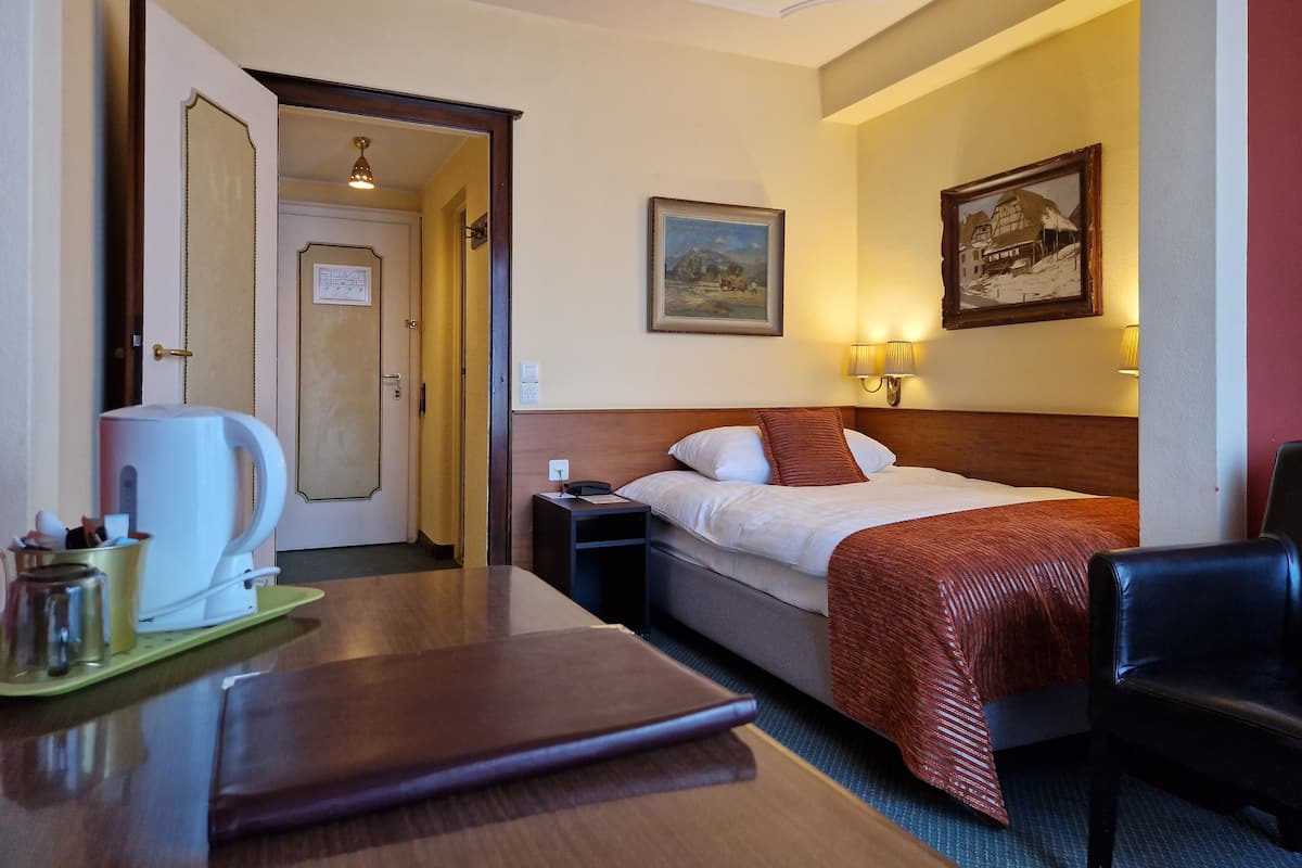 Una habitación de hotel con cama, mesita de noche, lámpara y un cuadro en la pared.