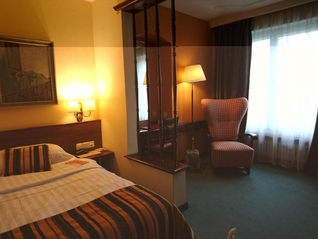 A hotel room with a bed, a chair, a desk, and a lamp.
