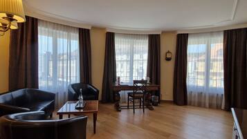 Una habitación de hotel con piso de madera, un sofá de cuero negro, una mesa de comedor con sillas y una lámpara.