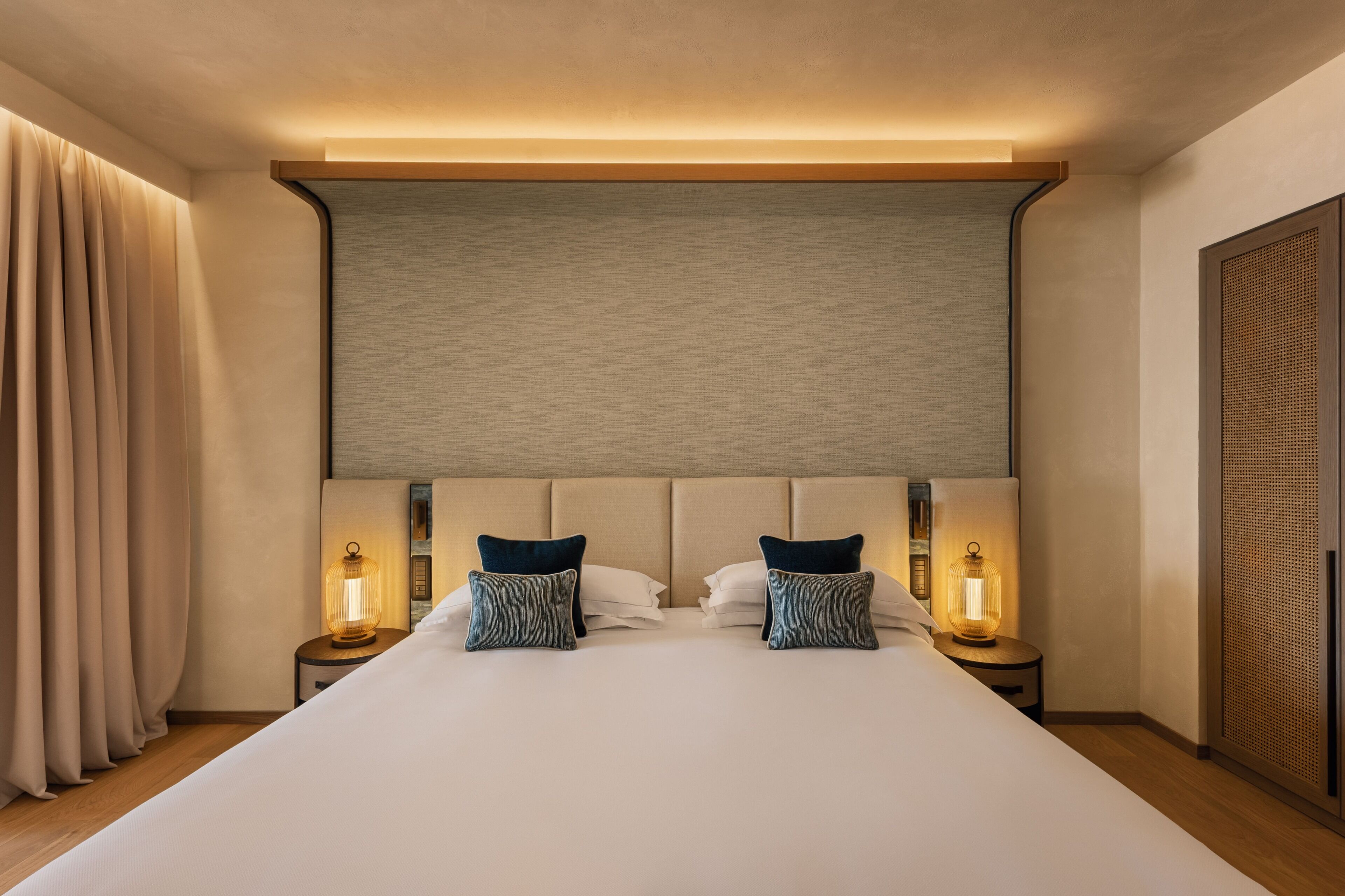 Una habitación de hotel con una cama grande, dos lámparas de noche, un cabecero y un armario.