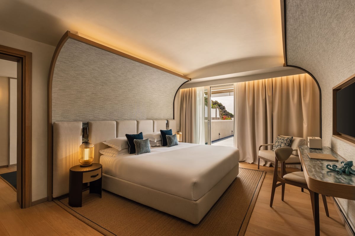 Une chambre d’hôtel moderne avec un grand lit, une table de chevet, une lampe et une vue sur l’extérieur.
