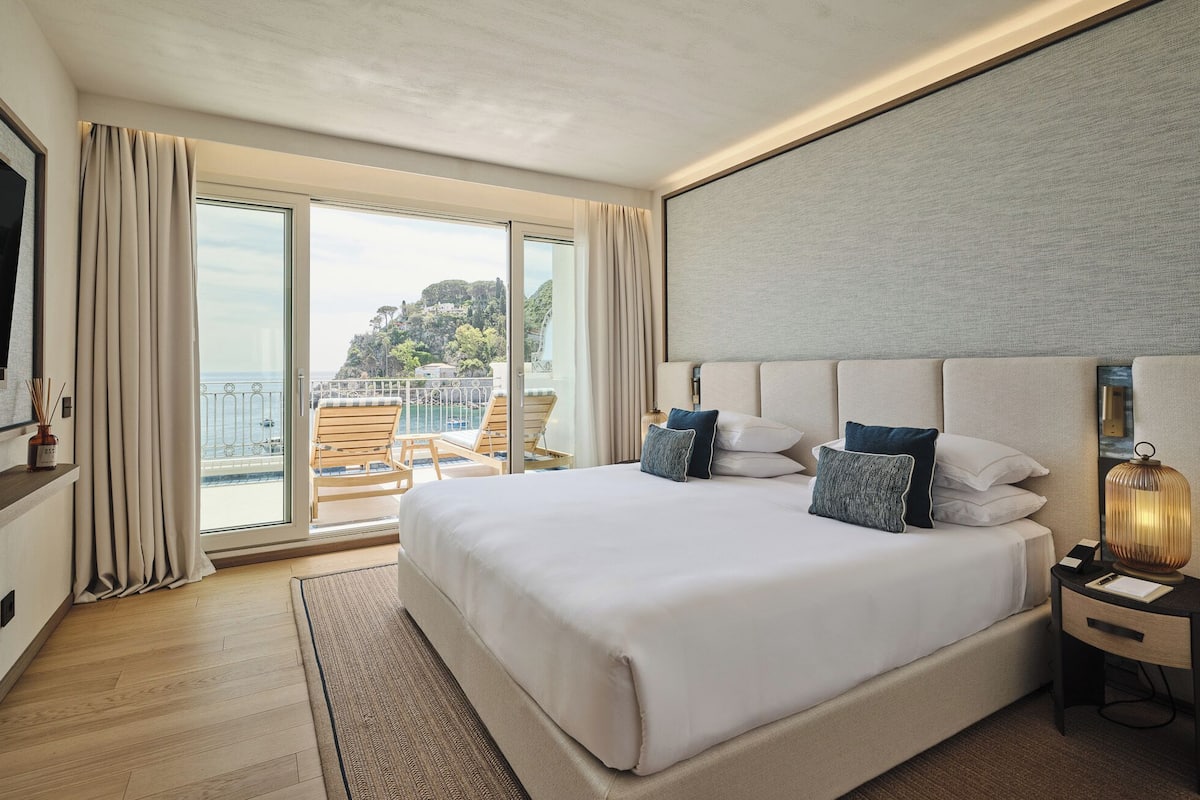Une chambre d’hôtel avec un grand lit, une télévision, un bureau et une vue sur la mer.