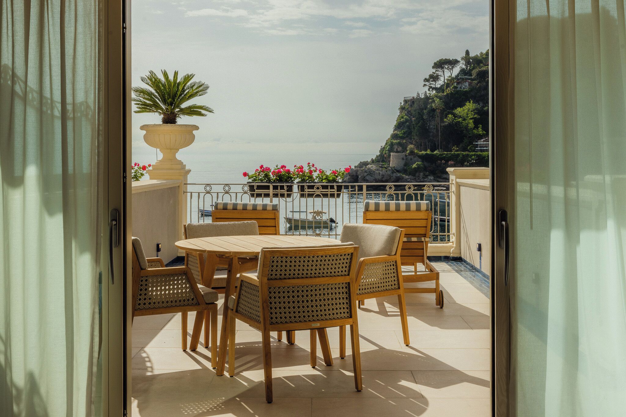 Een balkon met een tafel en stoelen, een bloempot en uitzicht op zee en een klif.
