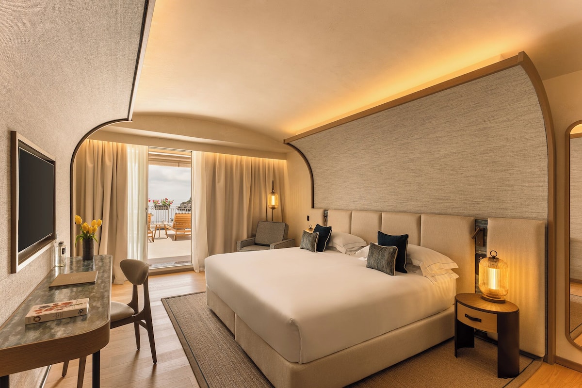 Une chambre d’hôtel moderne avec un grand lit, un bureau avec une chaise, une télévision et une fenêtre avec des rideaux.