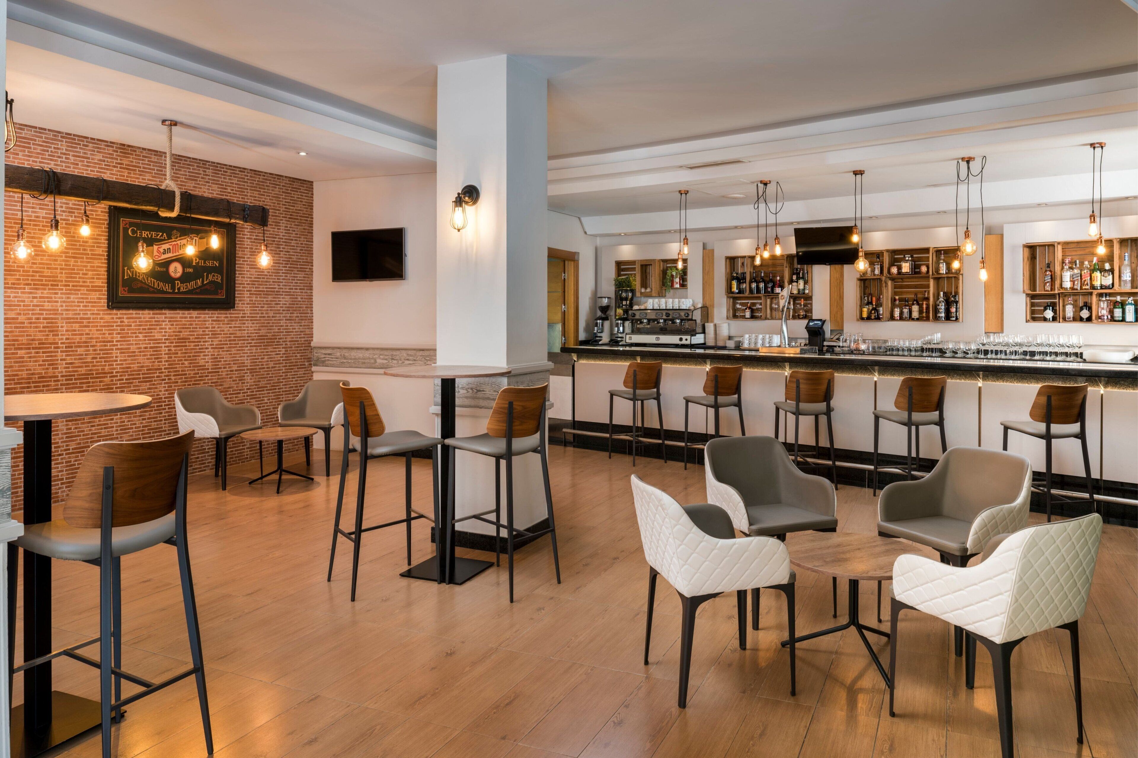 A modern bar area with wooden flooring, bar stools, and a variety of seating options including chairs and bar tables.
