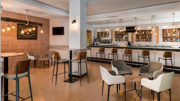 Een moderne barruimte met houten vloer, barstoelen en diverse zitmogelijkheden, waaronder stoelen en bar tafels.