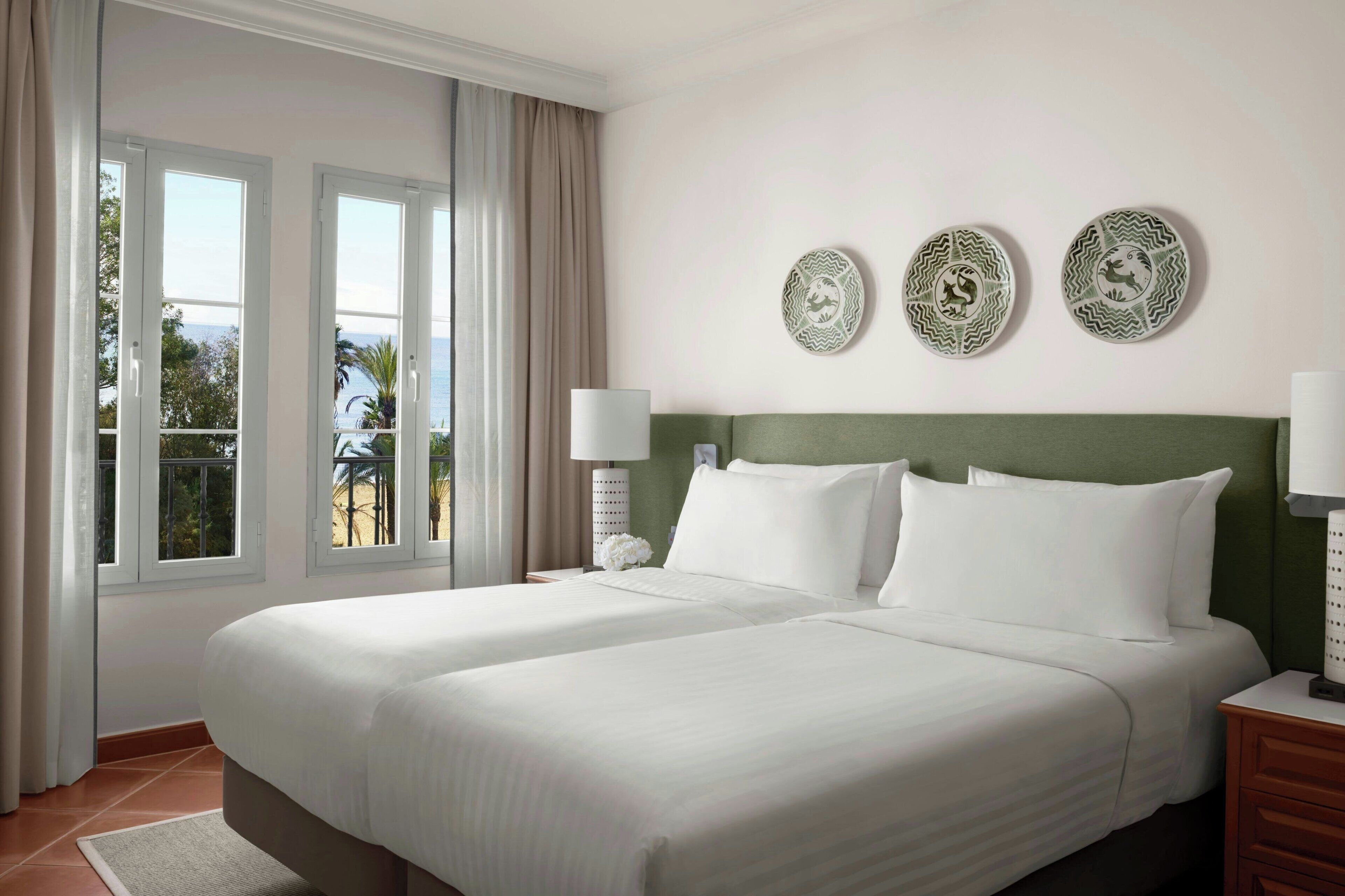 Una habitación de hotel con una cama grande, dos mesitas de noche, una ventana con cortinas y decoración en la pared.