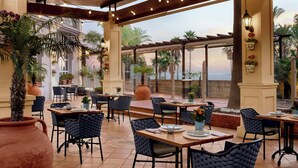 An outdoor patio area with tables and chairs, potted plants, and a view of the ocean. - Marriott's Playa Andaluza (Estepona)