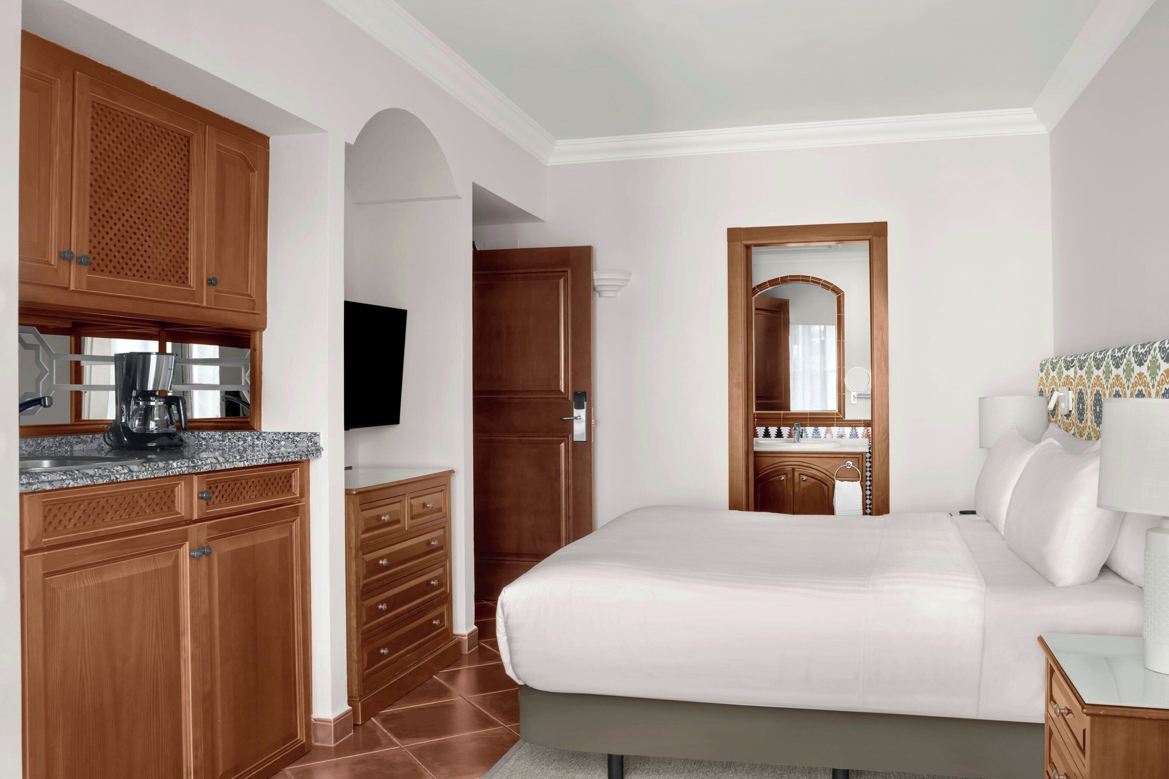 Een hotelkamer met een bed, een televisie, een houten kast en een badkamer met een spiegel.