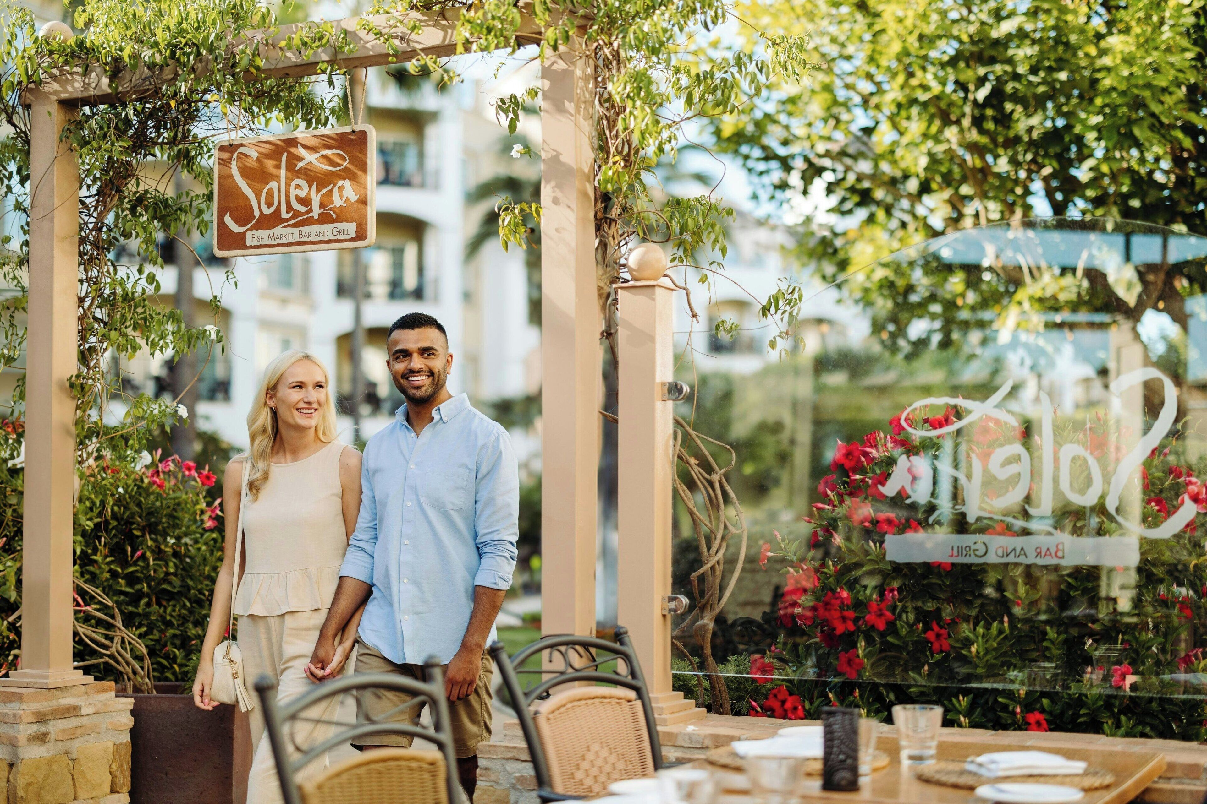A couple standing under a pergola with a sign that reads "Solera Fish Market Bar and Grill".