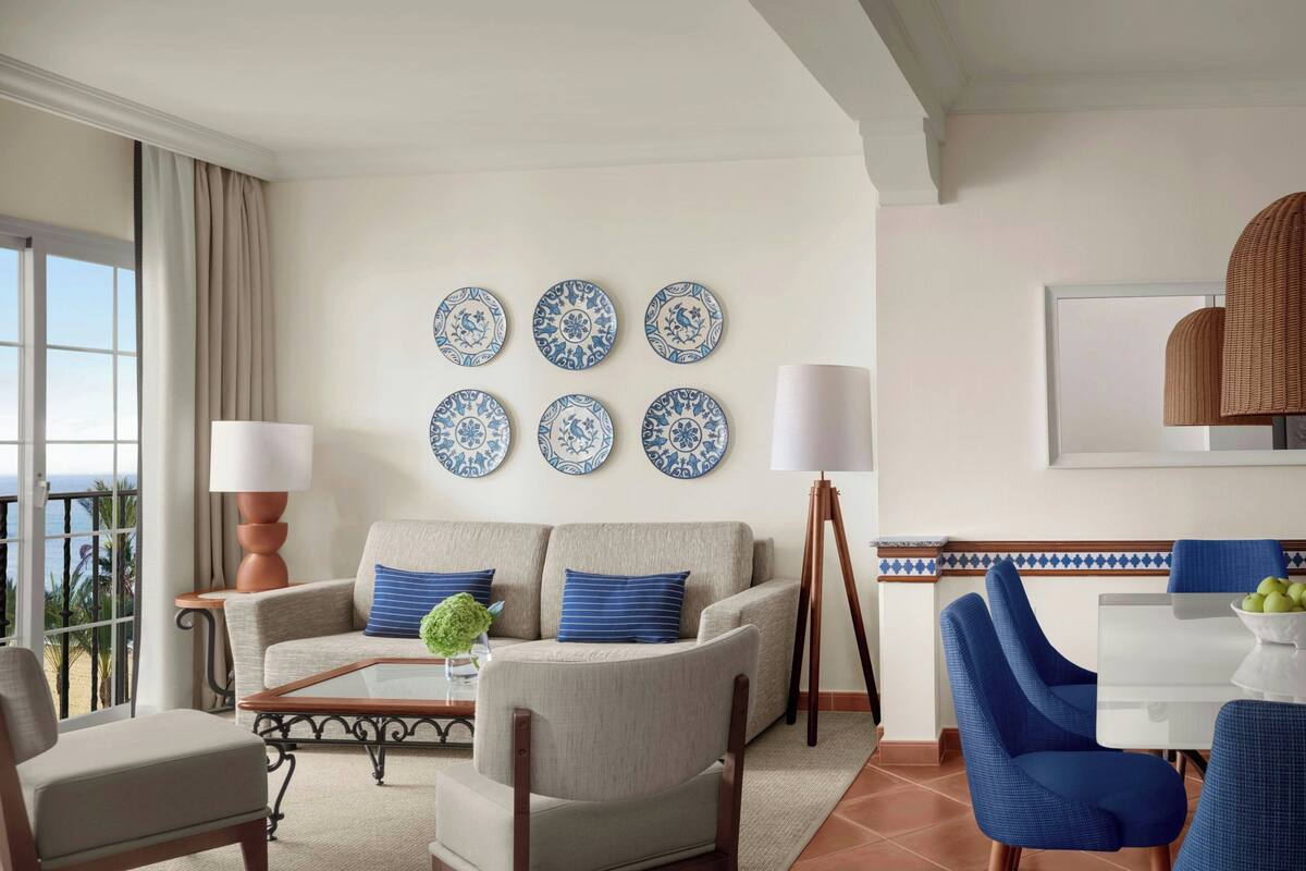 A living room with a sofa, chairs, a coffee table, a lamp, a dining table, and wall-mounted decorative plates.