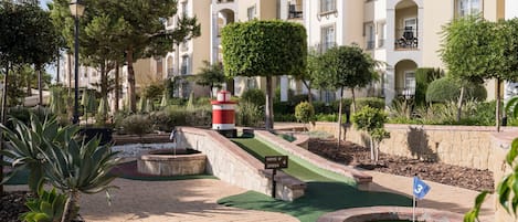 A golf course with a red and white lighthouse, surrounded by trees and a building with balconies.