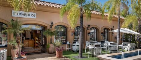 A storefront with a sign reading "The Marketplace," outdoor seating with umbrellas, and a small pool.