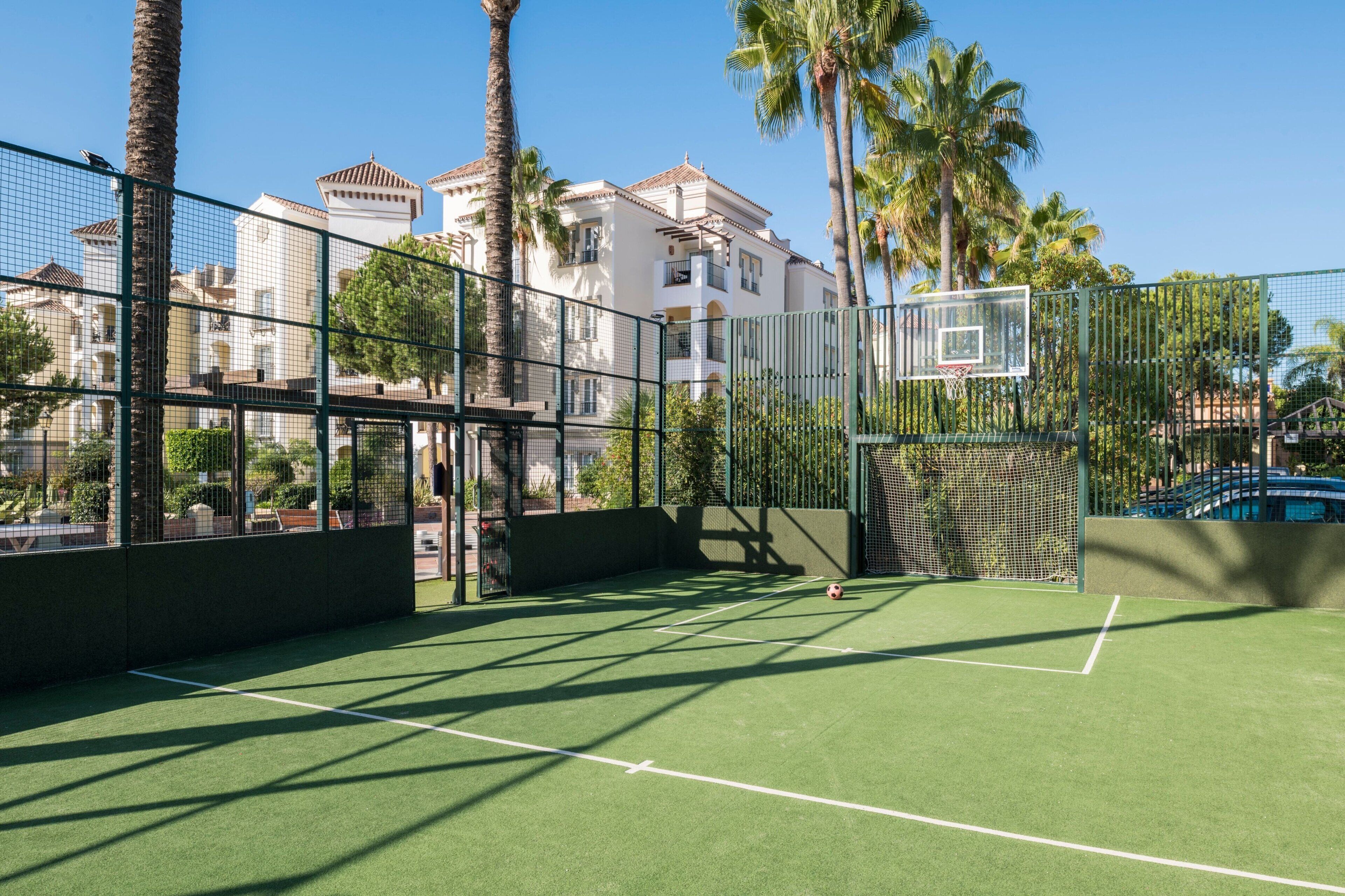 Ein Tennisplatz mit Netz, umzäunt und von Palmen gesäumt.
