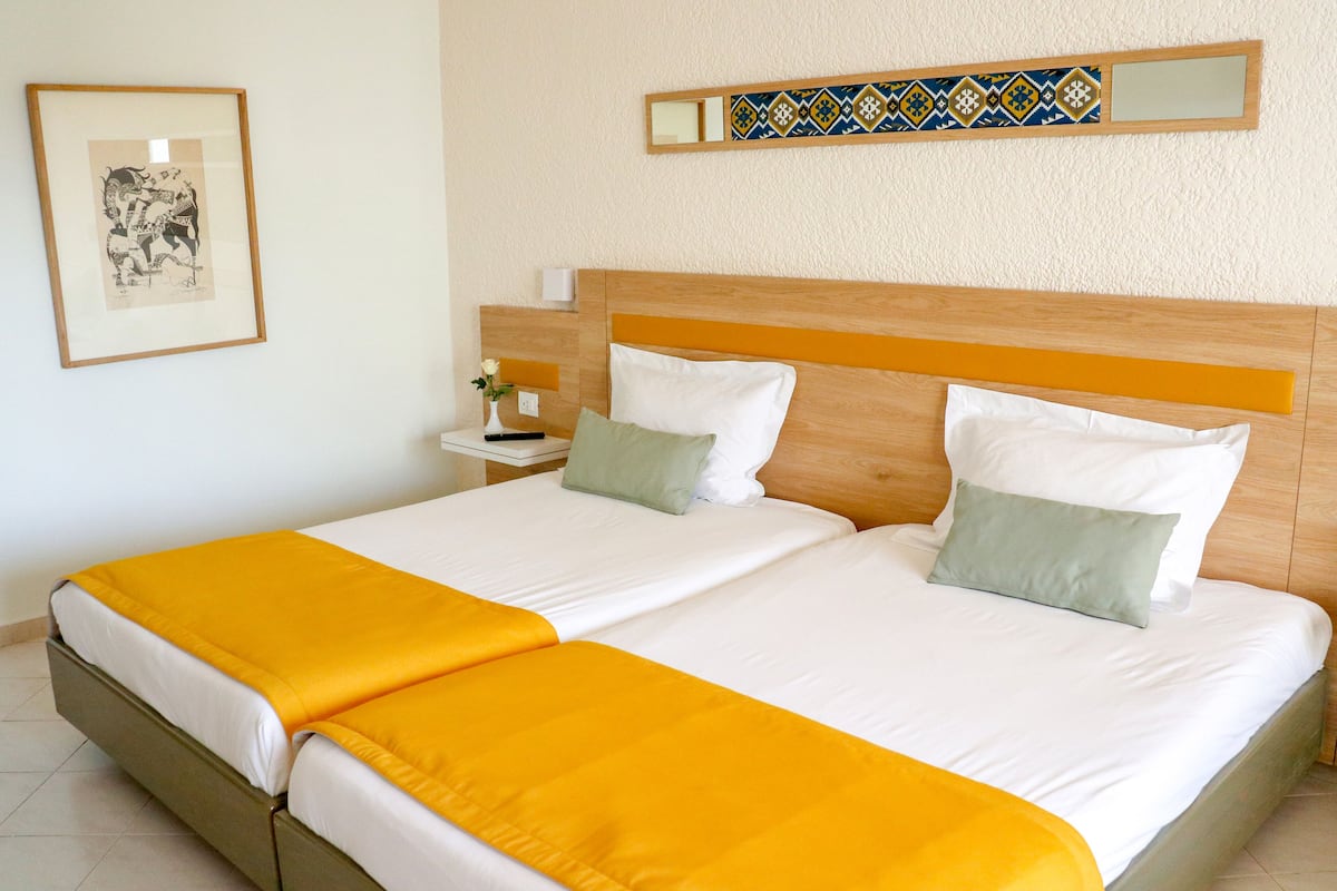 Een tweepersoonsbed met twee kussens, een nachtkastje met een lamp en een lijst met een afbeelding aan de muur.