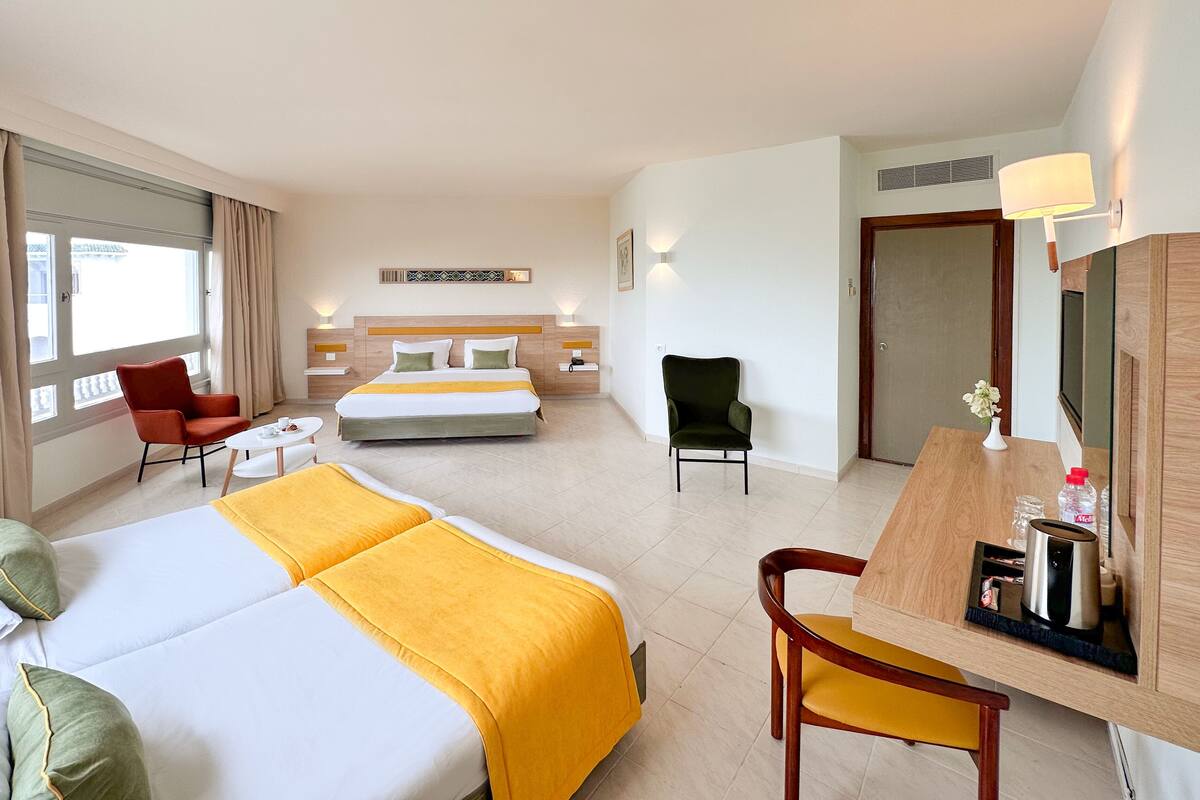 Een hotelkamer met twee bedden, een bureau, een stoel, een kleine tafel en een raam met gordijnen.