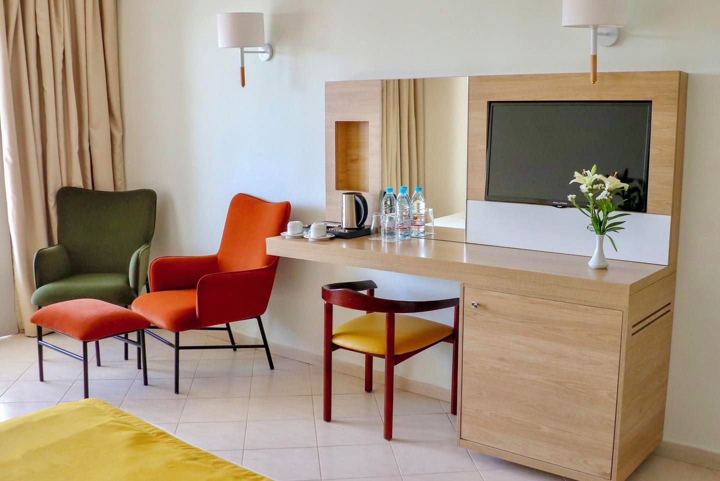 A hotel room with a desk, two chairs, a bed, a TV, and a coffee maker.