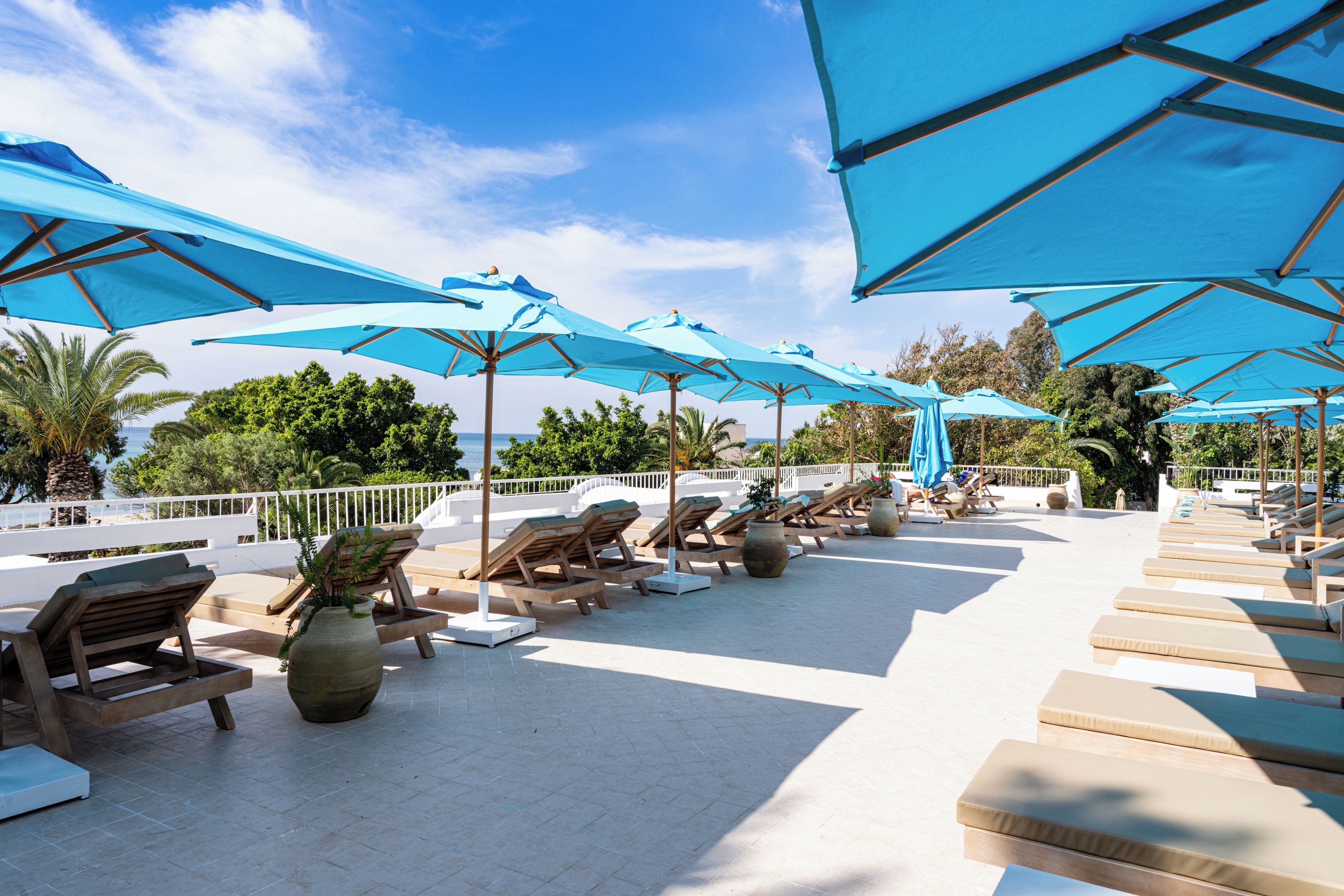 A sunlit outdoor seating area with lounge chairs and umbrellas, overlooking a body of water.