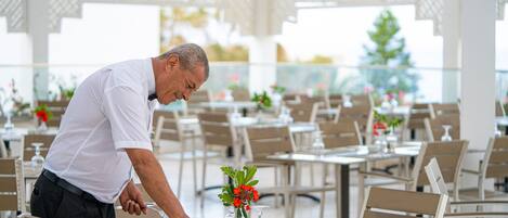 Ein Mann deckt einen Tisch in einem Restaurant ein, das mehrere Tische und Stühle bietet, mit einer dekorativen Vase und Blumen auf dem Tisch.