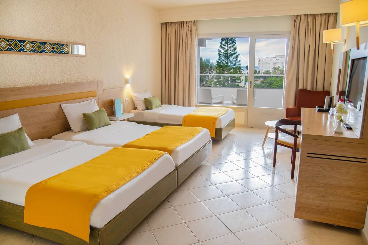 Een hotelkamer met twee bedden, een bureau, een stoel en een balkon met uitzicht.