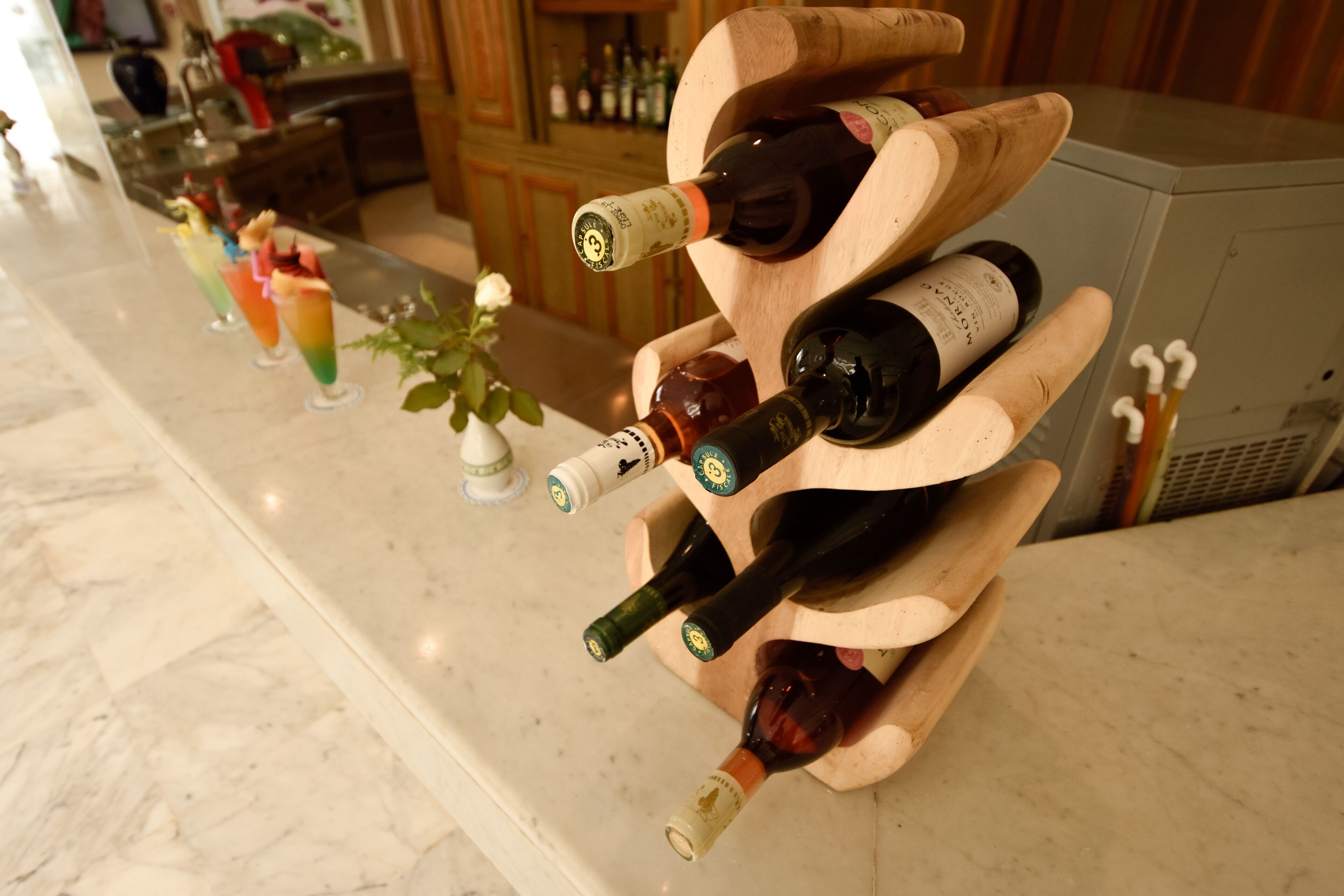 A wine rack with multiple bottles and a row of colorful drinks on a marble countertop.