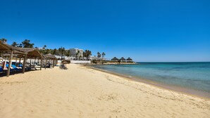 Una playa con tumbonas y sombrillas, cielo azul despejado y mar tranquilo.